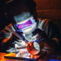 A man using a TIG (Tungsten Inert Gas) welder in a workshop.
