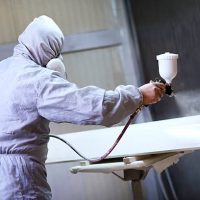 Mechanic in Painting Booth Spray Wooden Part of Furniture or hood of a car.
