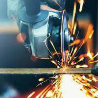 Closeup front view of unrecognizable man cutting thin metal rod with electric grinder. Usual day in a workshop. Sparks flying all over.