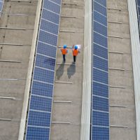 Aerial view of engineers walking on rooftop of a solar power plant.