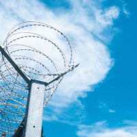 wirls of barbed wire over the fence. fence symbolizes prison, non-freedom, totalitarianism and prohibitions