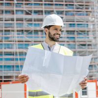 Civil engineer holding a technical drawing, he wears a reflective vest and helmet