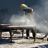 Man sand blasting a section of piping that belongs to a fishing boat. He is wearing protective gear to do his job.