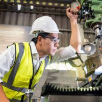 Asian Mechanical Engineer checking equipment in factory. factory workers using machine equipment in workshop. Asian mechanical engineer operating industrial lathe machine.